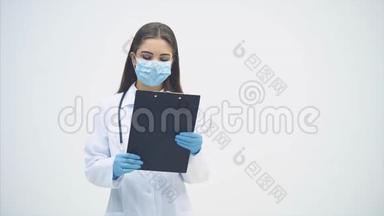 年轻的女<strong>实习生</strong>站在医疗制服和面具，拿着剪贴板，检查数据，摇头，翻转